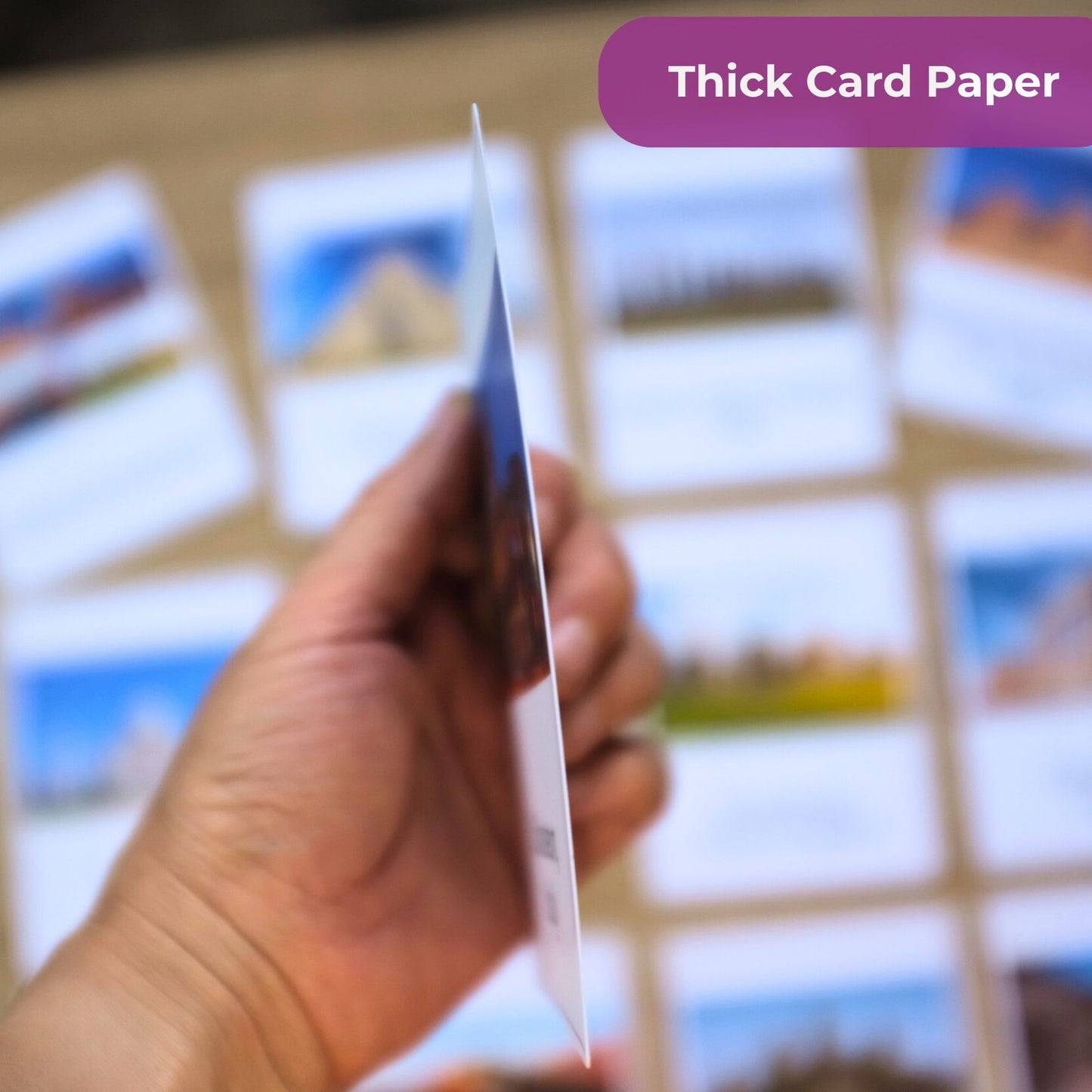 Hand holding a piece of thick card paper with blurred photo prints in the background